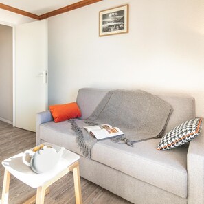 A neutral-colored sofa with a magazine, a teapot, and a cushion. A framed picture hangs on the wall above. - Wifi, 100m from ski slopes, swimming pool, sauna, balcony, ski locker, 28-32m², Alpe d'Huez (L'Alpe d'Huez)