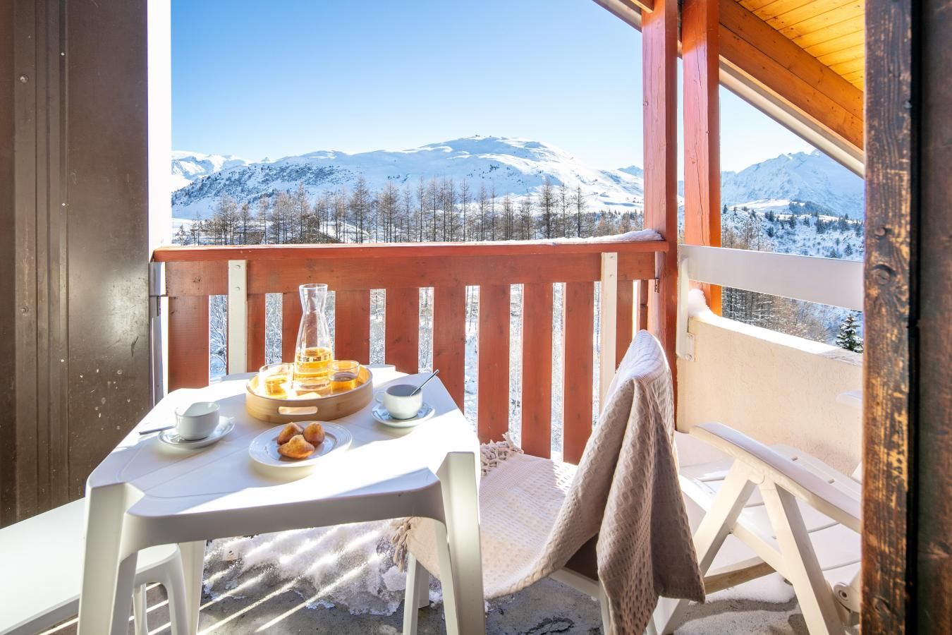 A balcony with a table set for breakfast, overlooking snow-covered mountains.