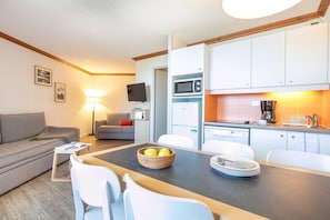 A compact living space with a sofa, a dining table with chairs, a kitchen area with appliances, and a flat-screen TV mounted on the wall. - Wifi, 100m from ski slopes, swimming pool, sauna, balcony, ski locker, 38m², Alpe d'Huez (L'Alpe d'Huez)