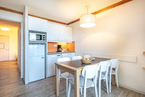A compact kitchen with a dining area, white appliances, and a wooden ceiling beam. - Wifi, 100m from ski slopes, swimming pool, sauna, balcony, ski locker, 38m², Alpe d'Huez (L'Alpe d'Huez)