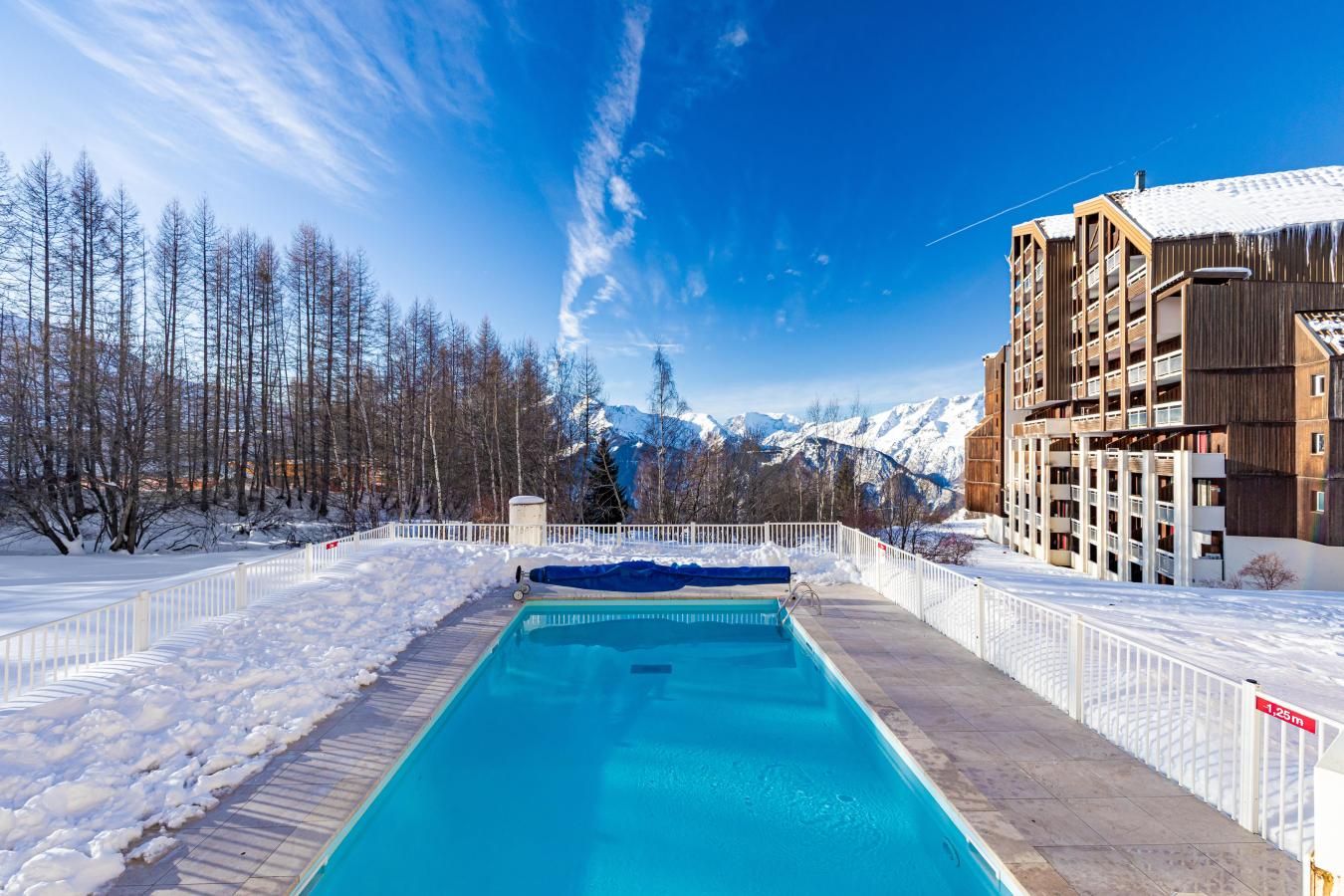 A swimming pool with a view of snow-covered mountains and a building with balconies.