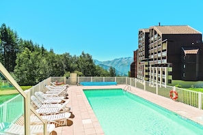A swimming pool with lounge chairs, a clear view of mountains, and a building with balconies. - Wifi, 100m from ski slopes, swimming pool, sauna, balcony, ski locker, 38m², Alpe d'Huez (L'Alpe d'Huez)