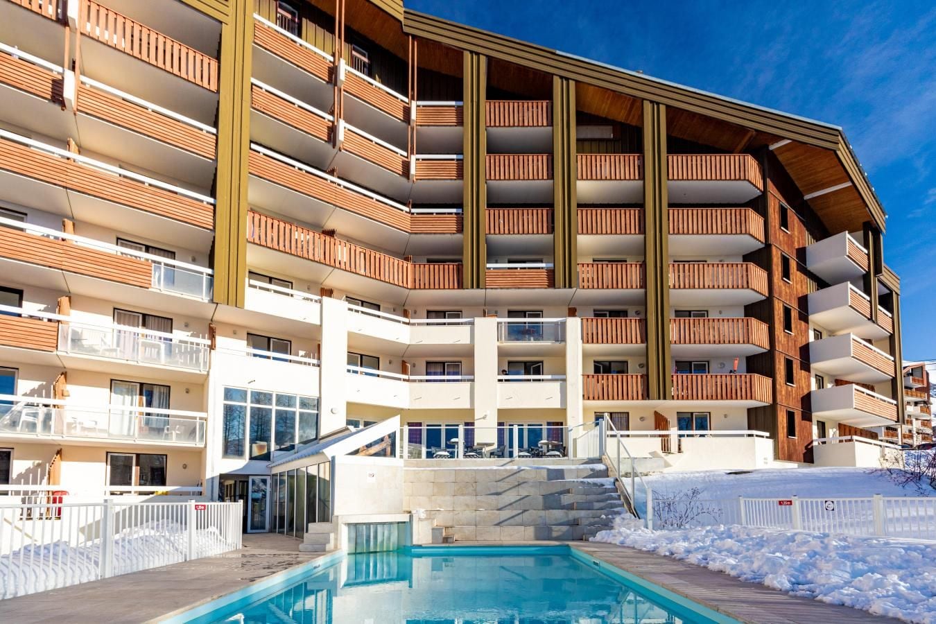 Un hôtel à plusieurs étages doté de balcons, d’une piscine et, au loin, d’une piste de ski.