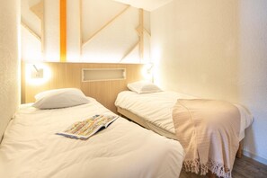 A hotel room with two beds, a wooden headboard, and a magazine on the left bed. - Wifi, 100m from ski slopes, swimming pool, sauna, balcony, ski locker, 40m², Alpe d'Huez (L'Alpe d'Huez)
