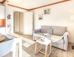 A living room with a sofa, a small table, and a kitchen area with cabinets and a countertop. - Wifi, 100m from ski slopes, swimming pool, sauna, balcony, ski locker, 40m², Alpe d'Huez (L'Alpe d'Huez)