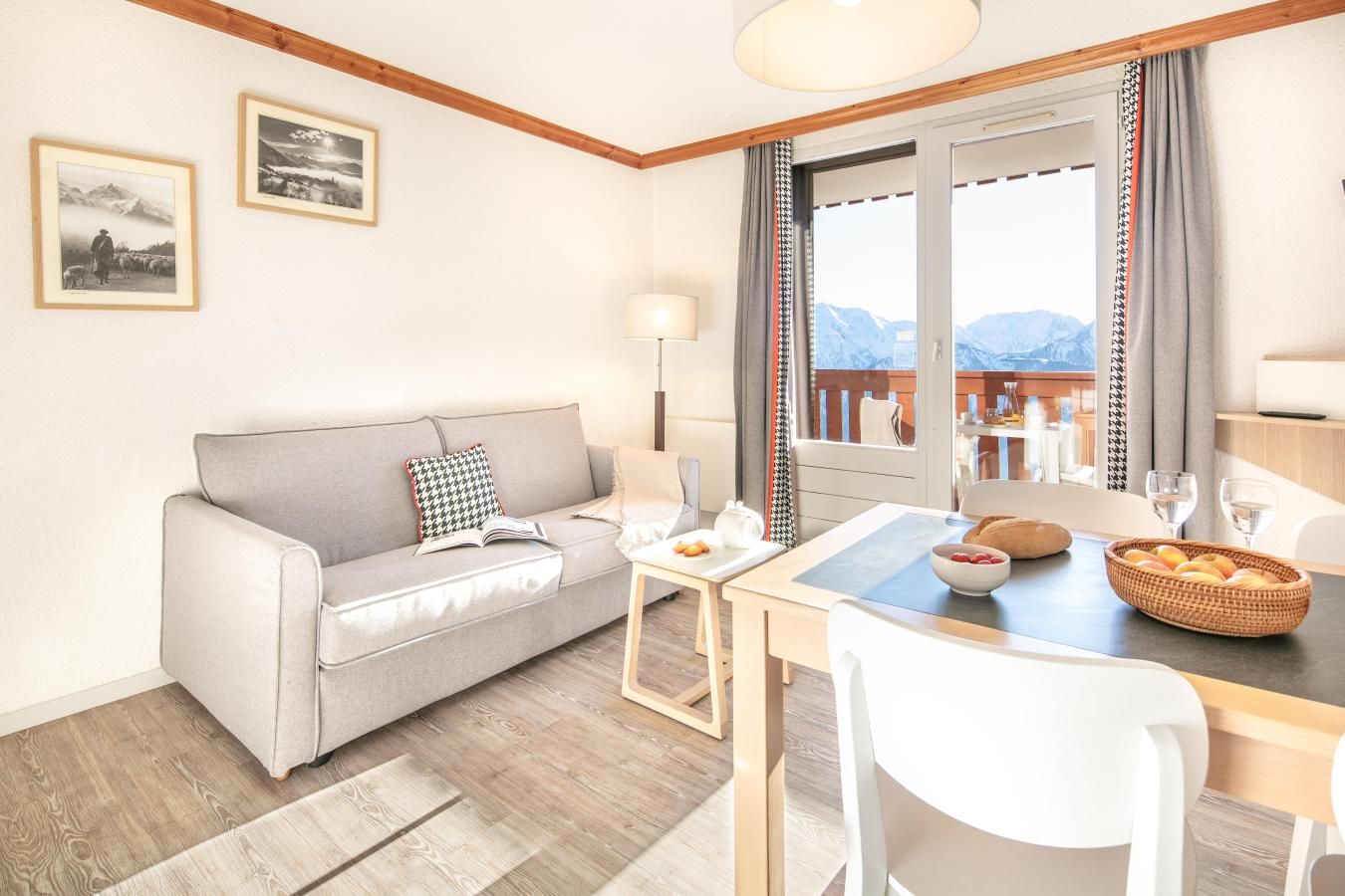 Une pièce chaleureuse avec un canapé, une table à manger et des chaises, une fenêtre avec des rideaux et deux tableaux encadrés accrochés au mur.