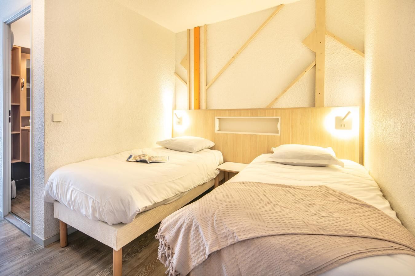 A hotel room with two beds, a wooden headboard, a bedside table, and a closet.
