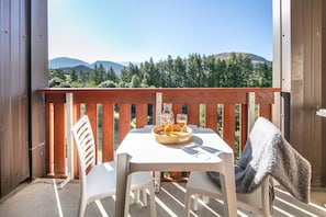 A balcony with a table set for two, a chair, and a view of a forested mountain range. - Wifi, 100m from ski slopes, Ground floor, swimming pool, sauna, balcony, ski locker, 40m² (L'Alpe d'Huez)