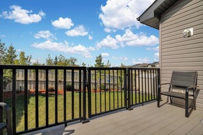 Eine Terrasse mit Metallgeländer, einem Stuhl und Blick auf einen Garten mit Rasen und Bäumen.