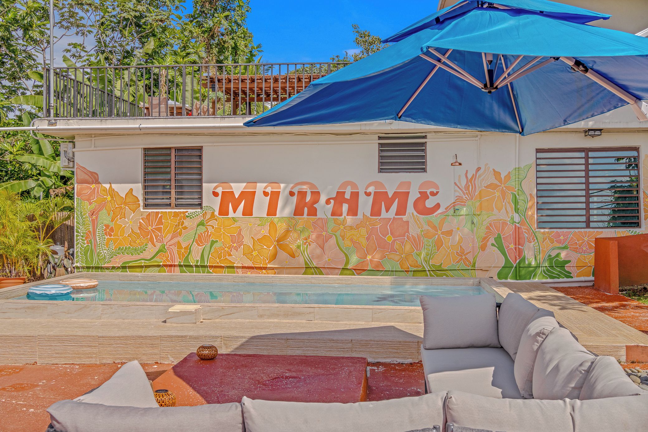 A pool area with a colorful mural, outdoor seating, and a large umbrella.
