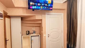 Une chambre d’hôtel équipée d’un téléviseur fixé au mur, d’une petite kitchenette avec un réfrigérateur, un four à micro-ondes et une machine à café.