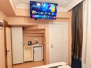 Habitació d'hotel amb televisió penjada a la paret, una cuineta petita amb nevera, microones i cafetera.