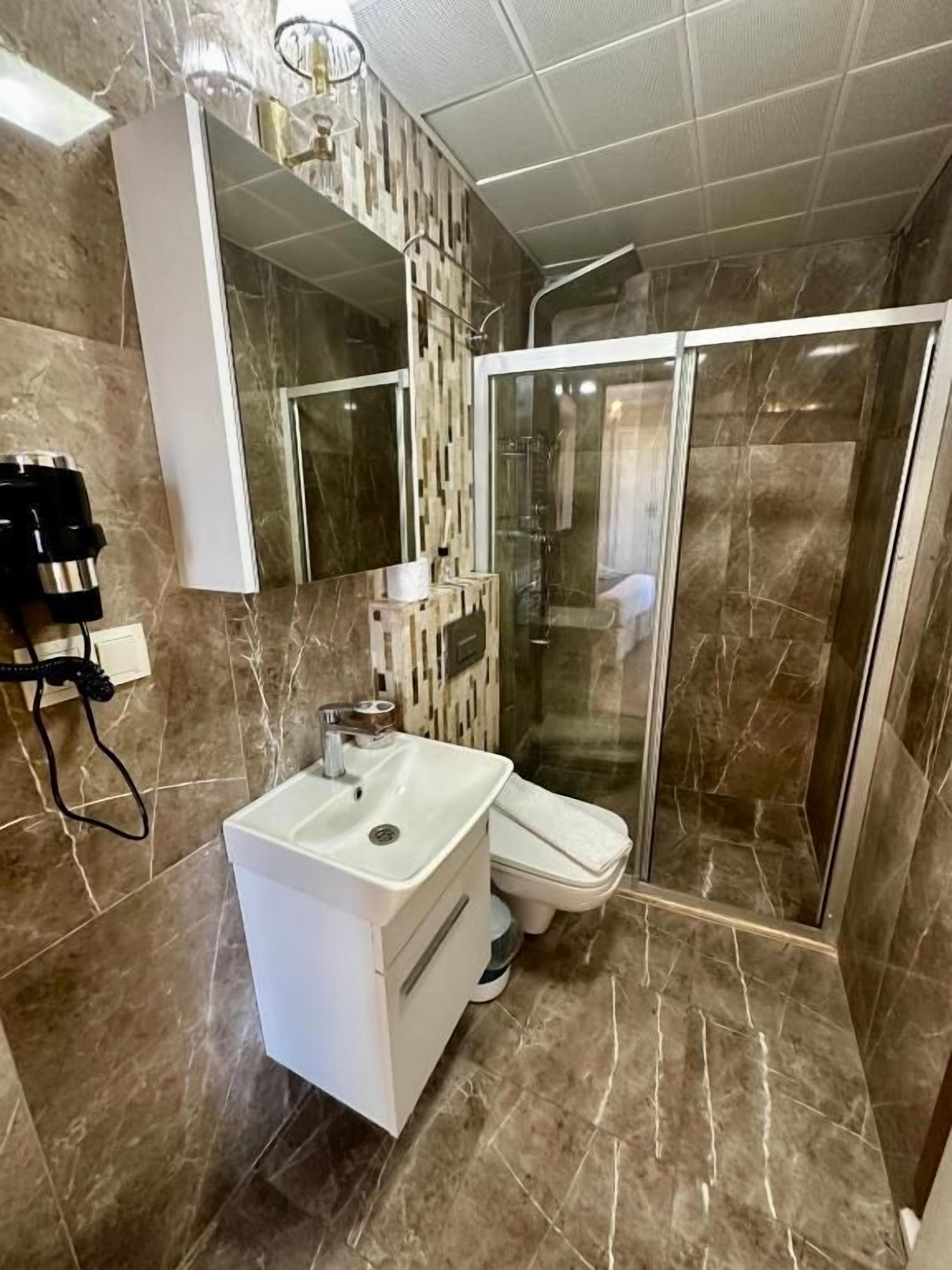 Une salle de bain avec un lavabo blanc, un miroir, un espace douche et un revêtement de sol en marbre.