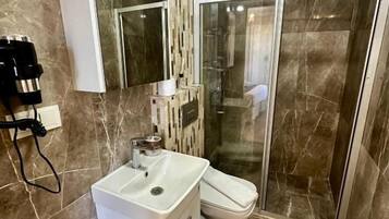 Une salle de bain avec un lavabo blanc, un miroir, un espace douche et un revêtement de sol en marbre.