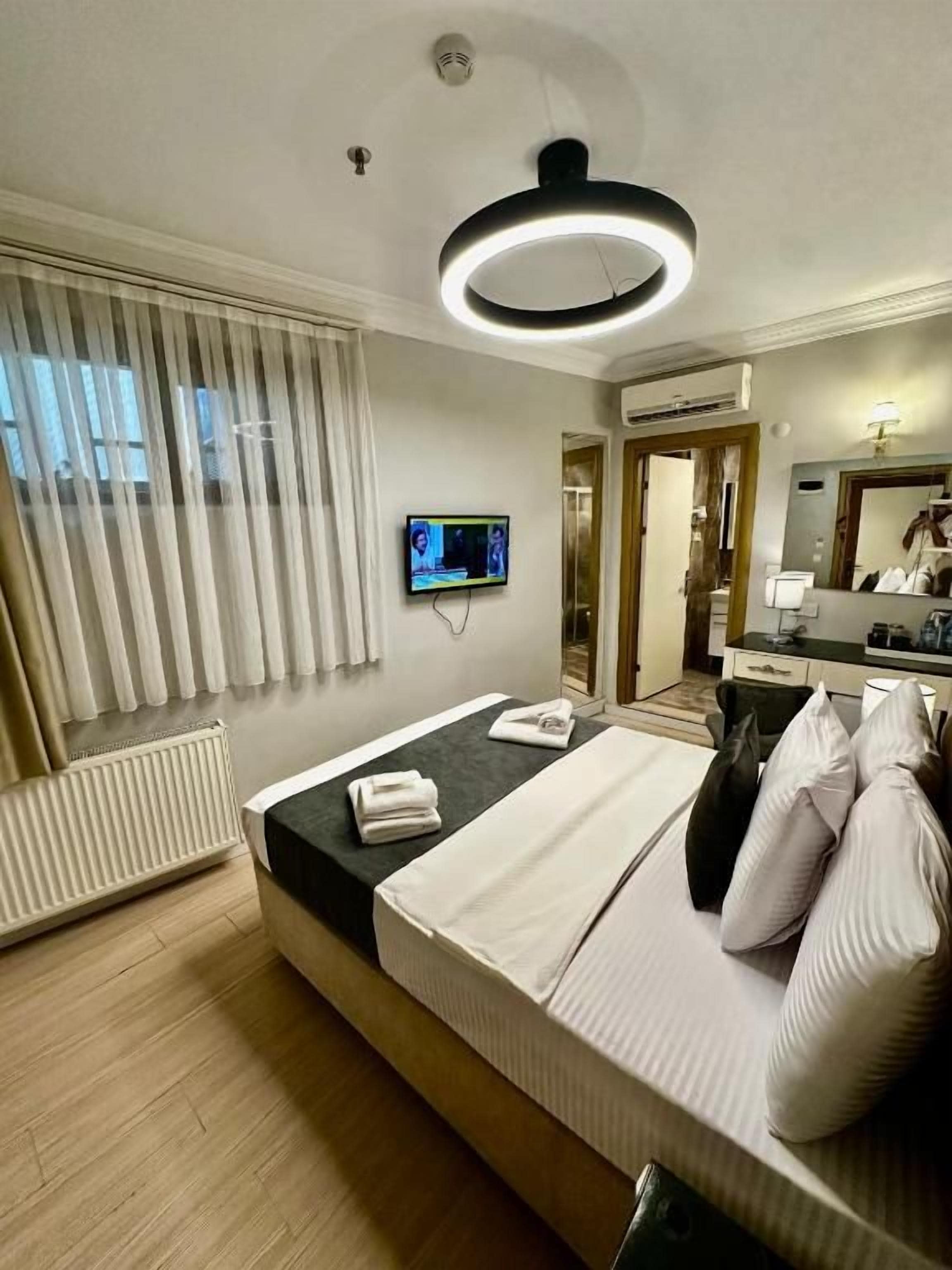 Ein Hotelzimmer mit einem Bett, einem Fernseher, einem Spiegel und einem Fenster mit Jalousien.