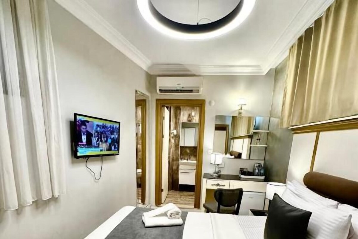 Ein Hotelzimmer mit Bett, Fernseher, Schreibtisch und einem durch eine offene Tür einsehbaren Badezimmer.