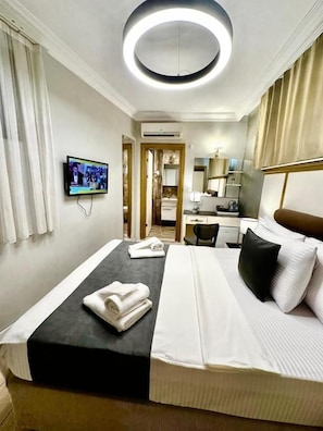 Ein Hotelzimmer mit Bett, Fernseher, Schreibtisch und einem durch eine offene Tür einsehbaren Badezimmer.