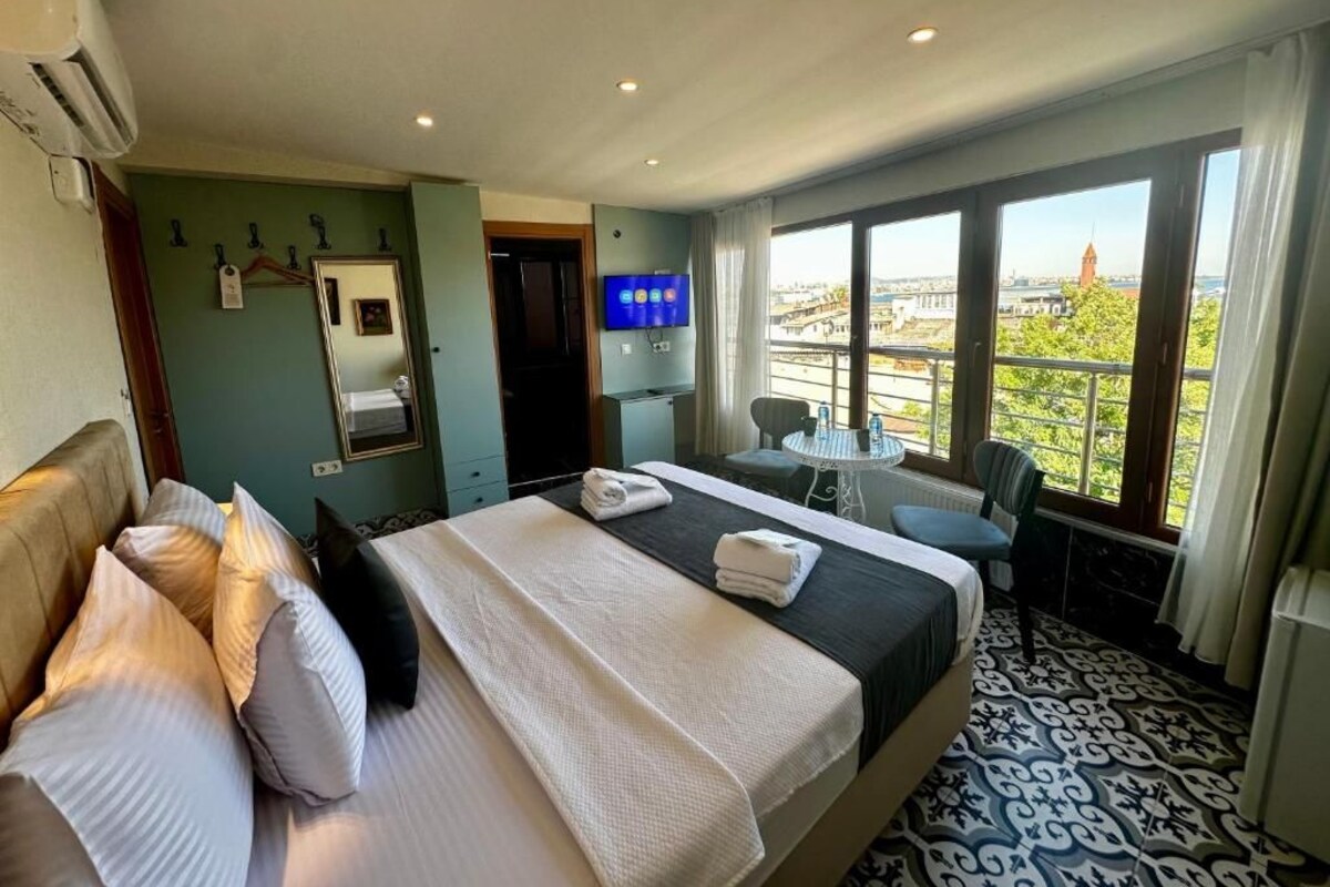 Ein Hotelzimmer mit Bett, Schreibtisch, Stuhl, Fernseher und einem Balkon mit Blick auf die Stadt.