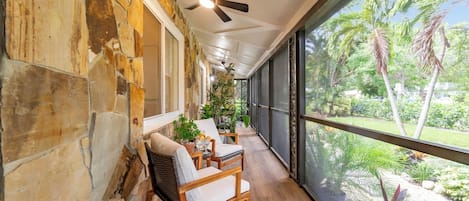 A covered outdoor seating area with stone walls, wooden furniture, and a view of tropical vegetation.