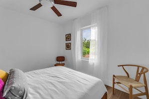 A bedroom with a bed, a wooden chair, a ceiling fan, and a window with curtains. - Tropical Oasis - 3BR, 10 Min Bal Harbour- Parking (Biscayne Park)