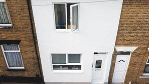 A two-story building with a white facade, a visible window with a curtain, and a door with a small window.