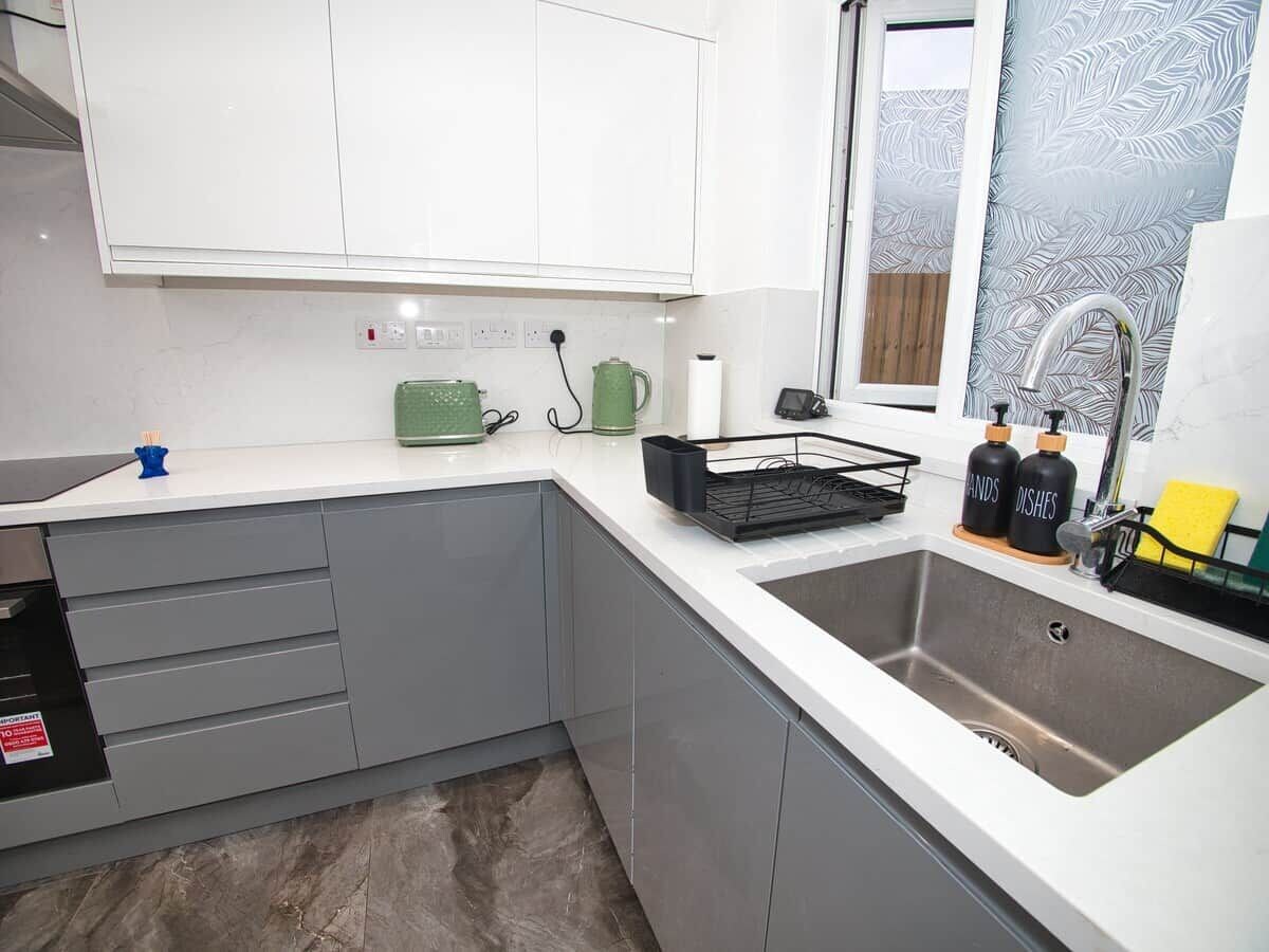 A modern kitchen with grey cabinets, a stainless steel sink, and a window with frosted glass.