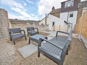 An outdoor seating area with benches and a table, surrounded by a wooden fence and a building with a white facade.