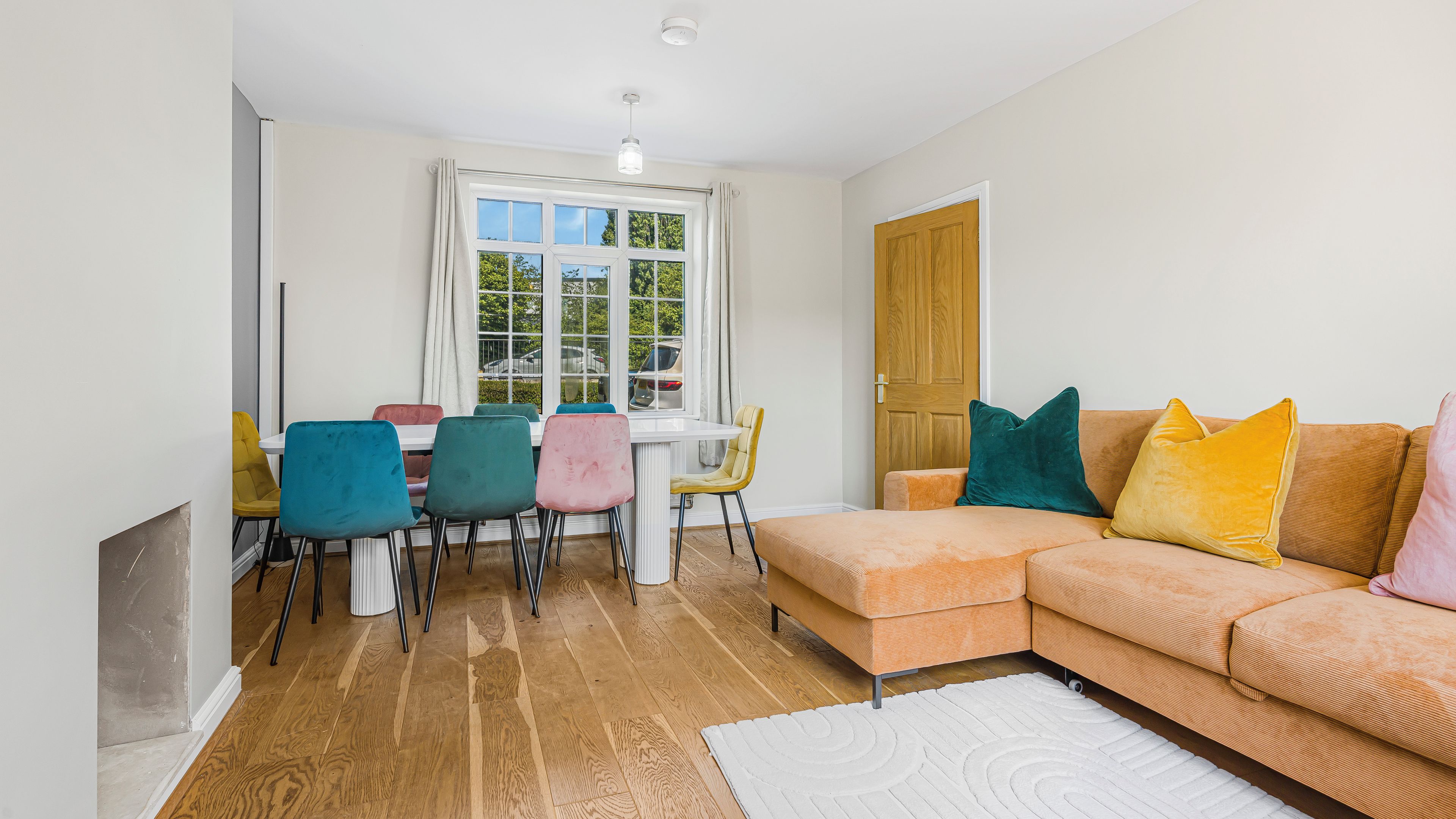 A living room with a sofa, chairs, a dining table, and a window with curtains.