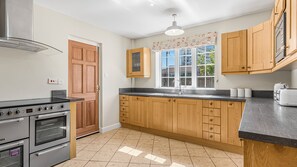 A kitchen with wooden cabinets, a built-in oven, and a window with a view of the outside. - Cosy 5BR House near NEC and BHX | Free parking (Birmingham)