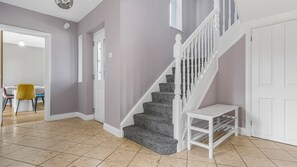 A staircase with a white railing, a small white bench, and a door with a light switch. - Cosy 5BR House near NEC and BHX | Free parking (Birmingham)