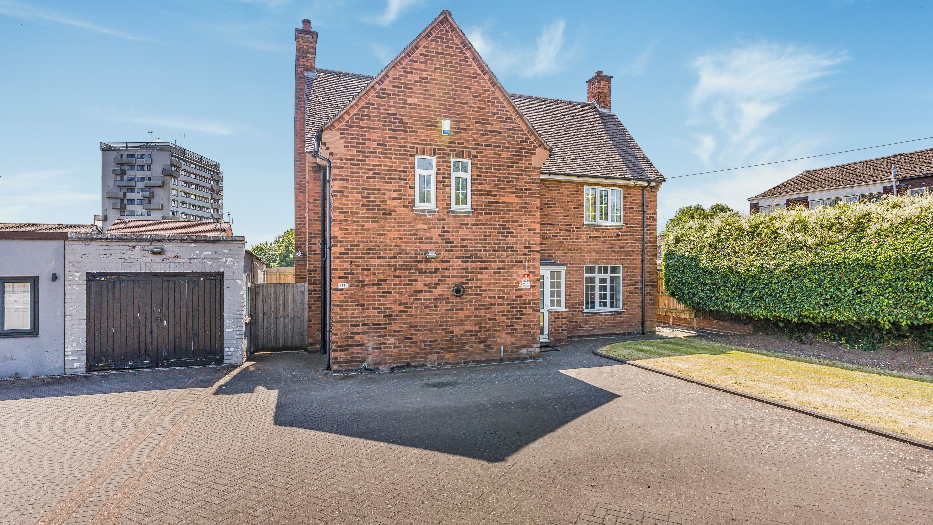 A two-story brick house with a pitched roof, a gated driveway, and a hedge.