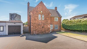 A two-story brick house with a pitched roof, a gated driveway, and a hedge. - Cosy 5BR House near NEC and BHX | Free parking (Birmingham)