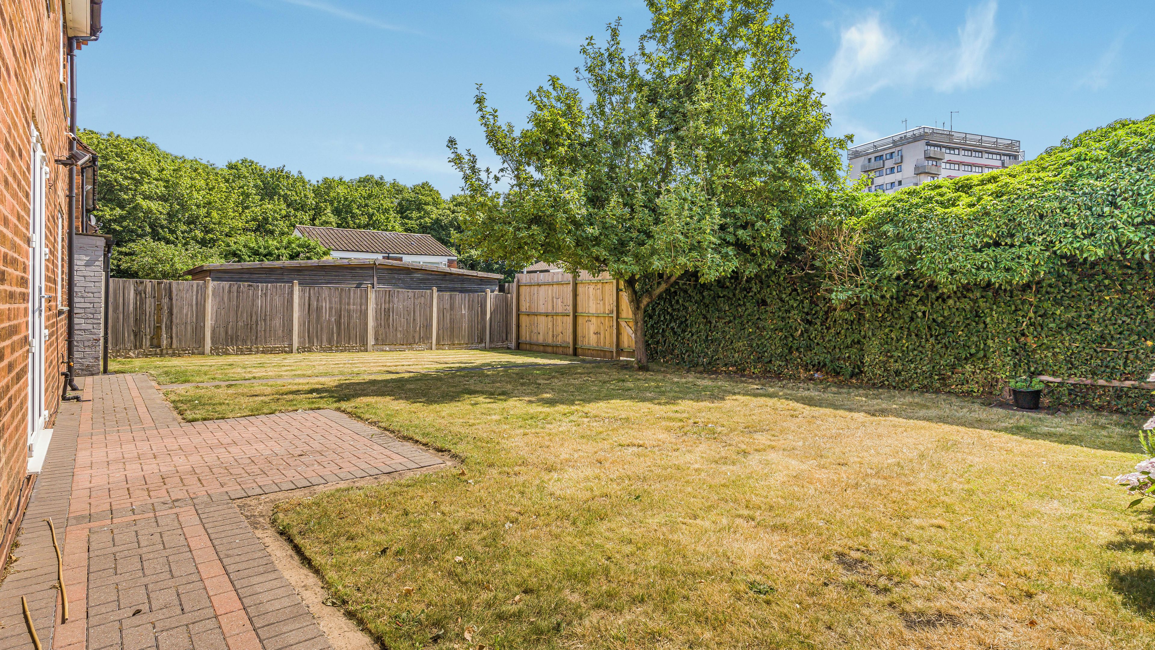 A backyard with a brick patio, a wooden fence, and a hedge.