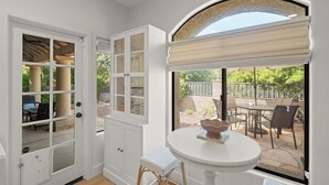 A room with a white door leading to an outdoor patio, a white table with a basket, and a window with a view of the patio. - Newly Renovated Foothills Home at the Base of the Catalina Mountains (Tucson)