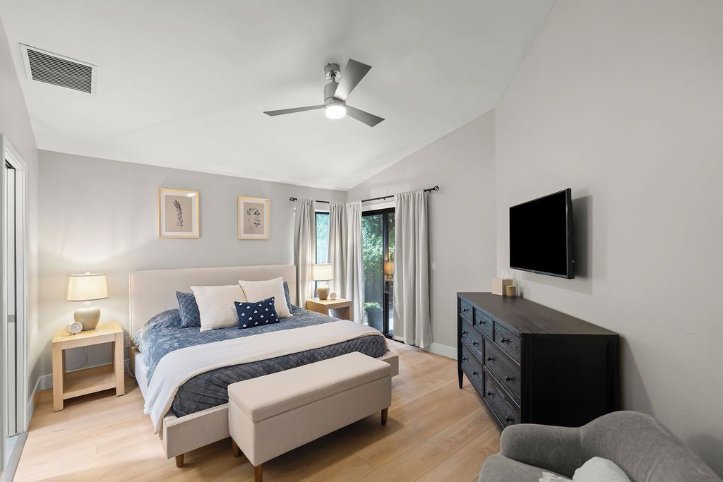 Ein Schlafzimmer mit Bett, Nachttischen, einem Schminktisch, einem Fernseher und einem Deckenventilator.