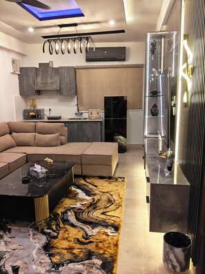 A modern living room with a sectional sofa, a marble coffee table, and a patterned rug. - 1BHK with luxury amenities (Islamabad)