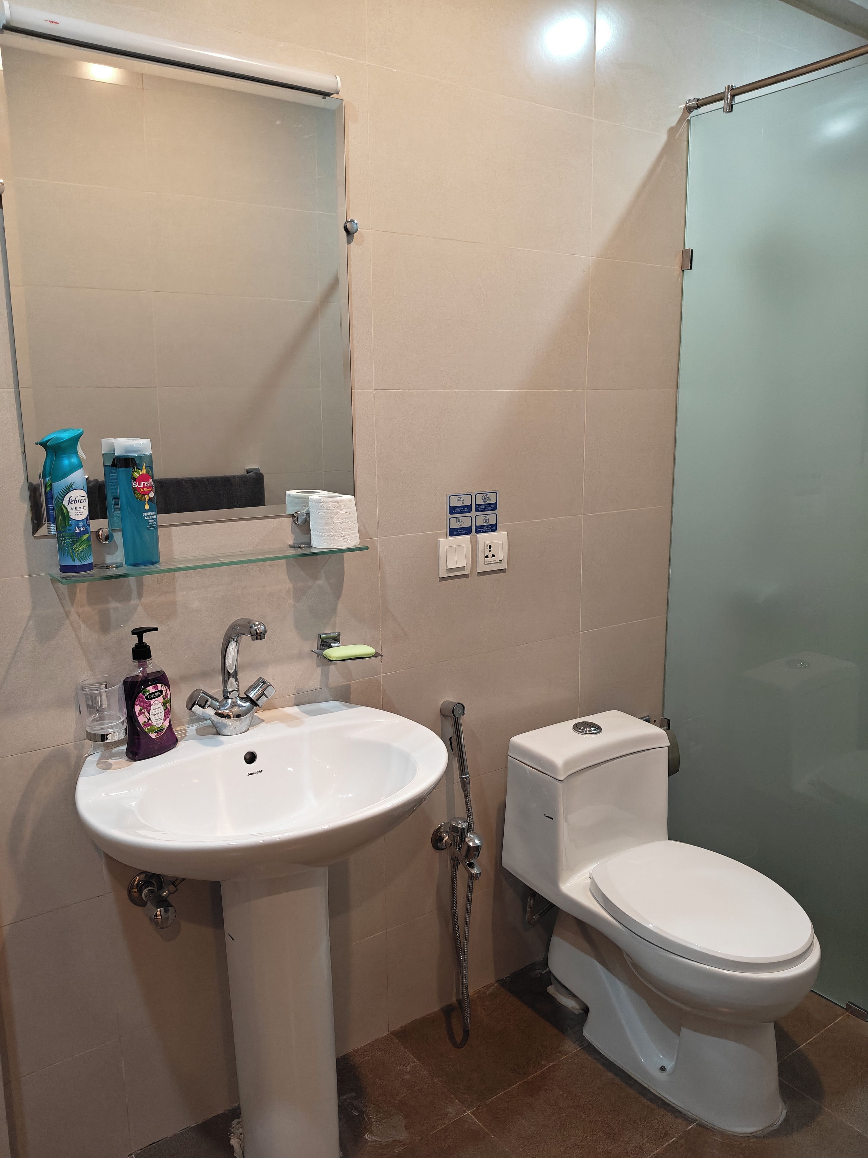 Une salle de bain avec un lavabo blanc, des toilettes, une douche en verre et un miroir au-dessus du lavabo.