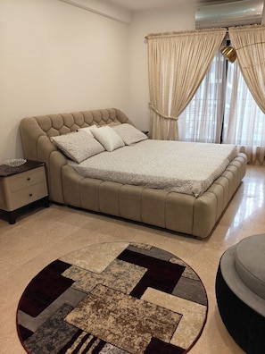 A bedroom with a large bed, a bedside table, a lamp, and a window with curtains. - 1BHK with luxury amenities (Islamabad)