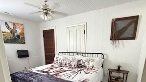 A bedroom with a bed, a ceiling fan, a wooden door, a small table, and a wall-mounted picture. - Escape to Gayles Farmhouse and discover your perfect mountain getaway. (Trenton)