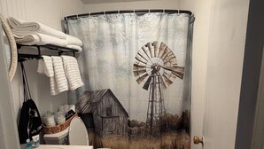 A bathroom with a farmhouse and windmill shower curtain, a toilet, and a sink with towels. - Escape to Gayles Farmhouse and discover your perfect mountain getaway. (Trenton)