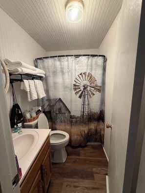 Un baño con cortina de ducha de granja y molino, un inodoro y un lavabo con toallas.