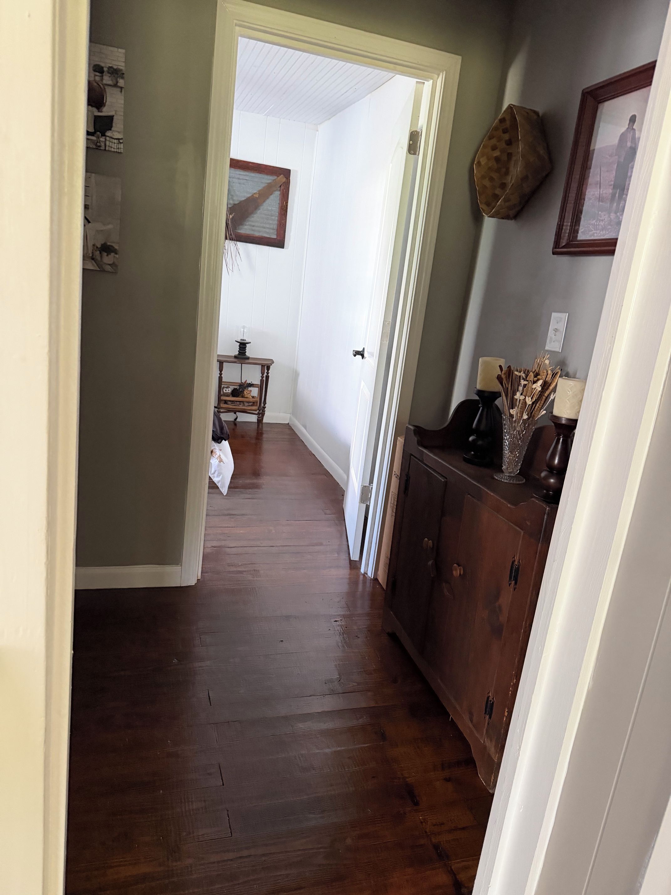 A hallway with wooden flooring, a white door, and a brown cabinet with decorative items.