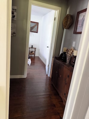 A hallway with wooden flooring, a white door, and a brown cabinet with decorative items.