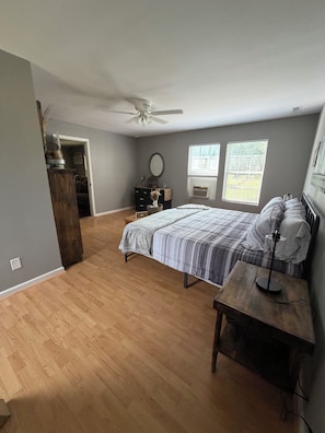 A bedroom with a bed, a nightstand, a dresser, a ceiling fan, and two windows.