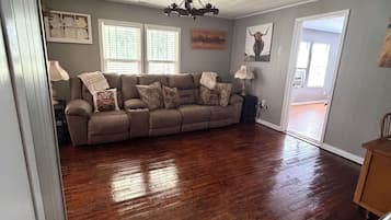 A spacious living room with a large sectional sofa, hardwood flooring, and a chandelier.