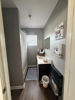 Un baño pequeño con ducha, lavamanos, espejo y ventana.