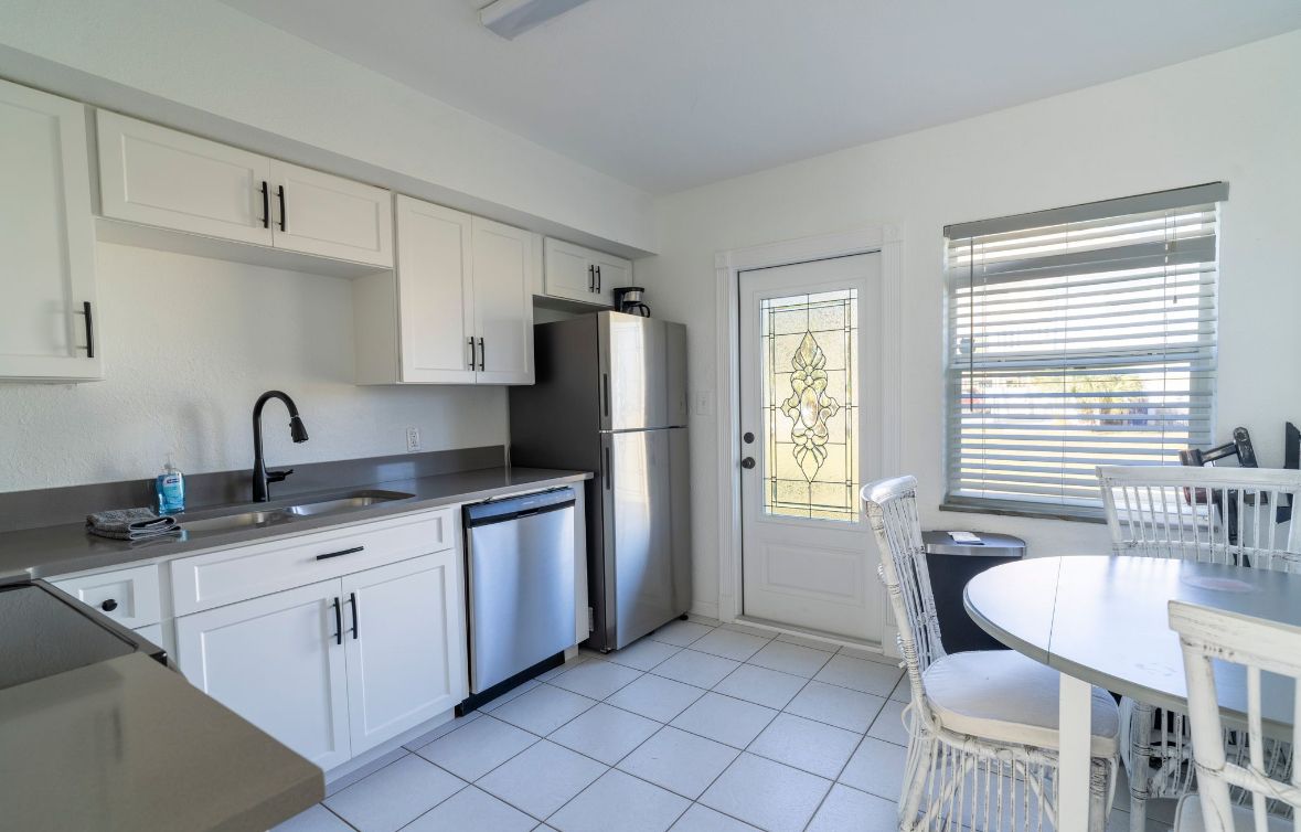 A modern kitchen with white cabinets, stainless steel appliances, and a dining area with white chairs.