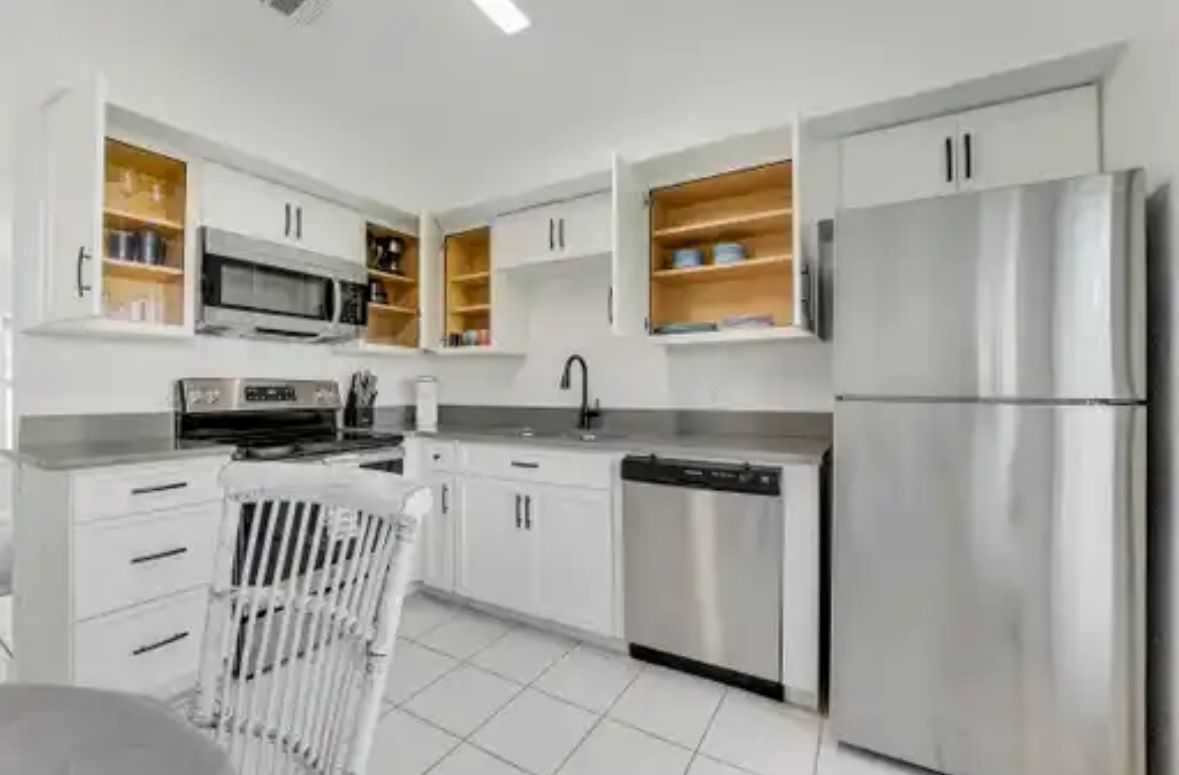 A modern kitchen with white cabinetry, stainless steel appliances, and open shelving.