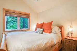 Une chambre à coucher avec un lit, une table de chevet, une lampe et une fenêtre donnant sur des arbres.