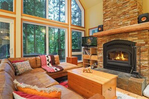 A cozy living room with a stone fireplace, leather sofa, and a bookshelf. - Cedar Hollow Mt Baker Cabin with Hot Tub and Stone Fireplace (Deming)
